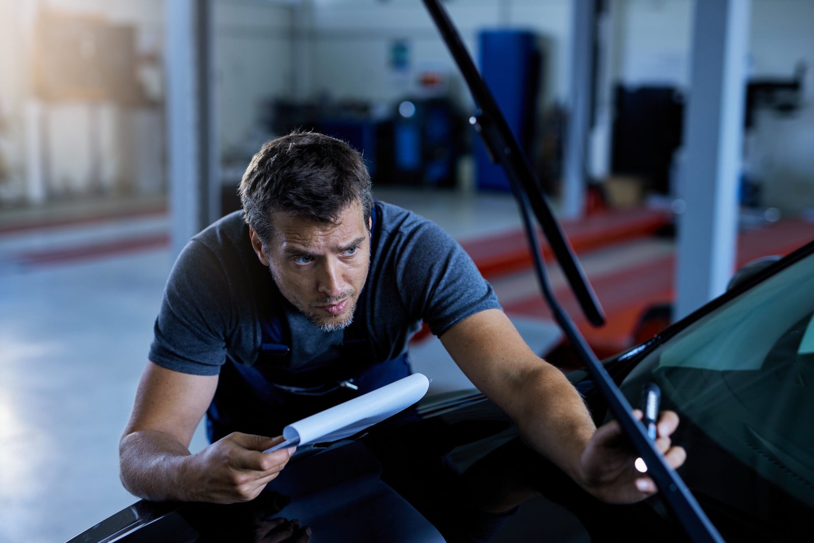 Home auto repairman examining a car while working at workshop.