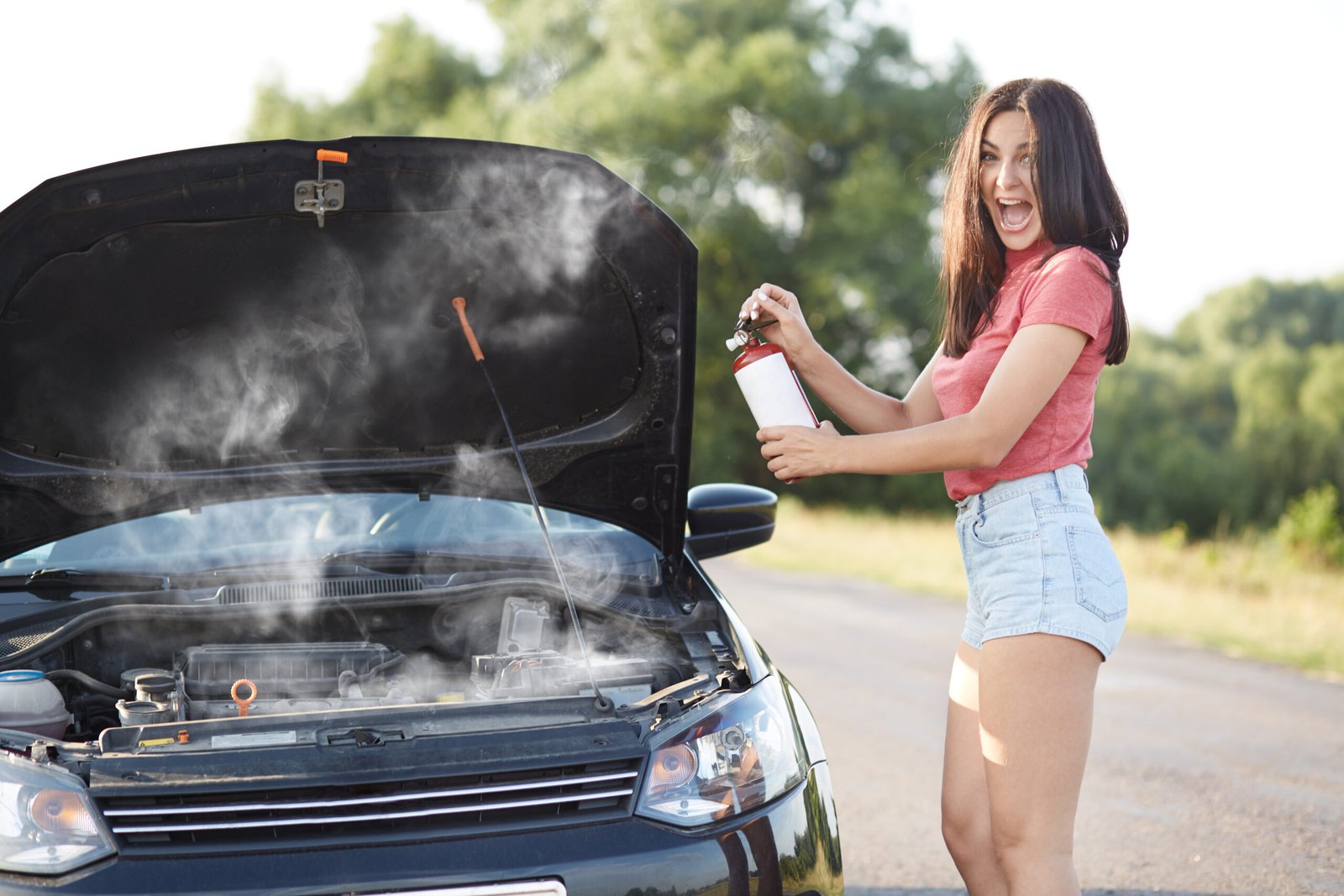 Home depressed brunette female driver stands near brocken car with opened hood, tries to solve technical problem by herself while waits for auto technician, opens mouth widely, exclaims in great despair