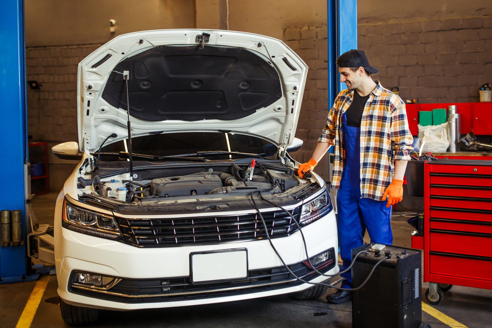 Home full length shot of handsome auto mechanic charging the battery using wire cables in modern service station